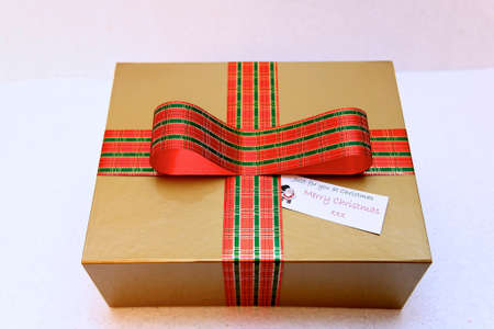 gold coloured rectangular gift box with tartan ribbon against a plain background.の写真素材