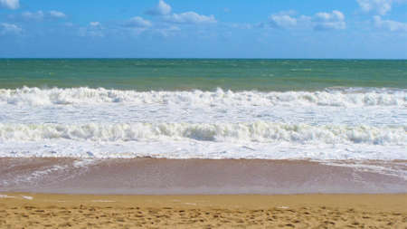 sandy beach with green sea and cloudy blue skies in the Algarve in Portugal.の写真素材