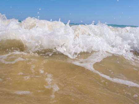 blurred effect of the incoming tide with sandy coloured bach below and blue sky aboveの写真素材