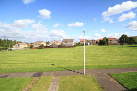 open grassy area under the sun and cloudy blue sky with lampo posts and houses in view.の写真素材