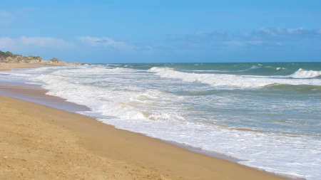 waves rolling in on the sandy shoreline of the beach under blue skies in the Algarve in Portugal.の写真素材