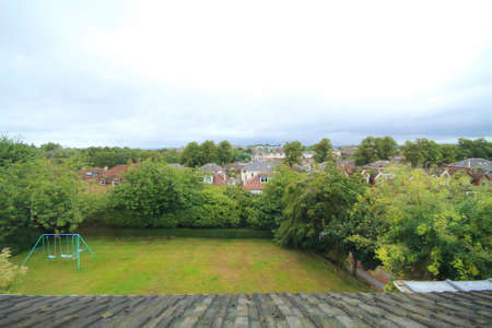 view of the garden and surrounding neighbourhood taken from the top floor showing grass, trees, a child's swing, houses and cloudy sky.の写真素材