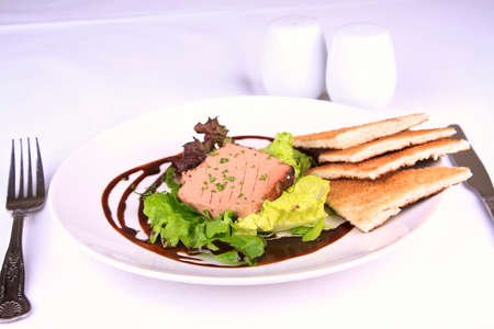 duck liver pate with melba toast, vinaigrette and lettuce on a white plate with cutlery and salt and pepper.の写真素材