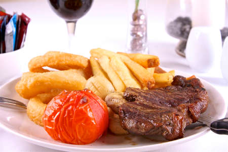 sirloin steak with mushrooms, grilled tomato, chips and onion rings with glass of wine and condiments in the baackground.の写真素材