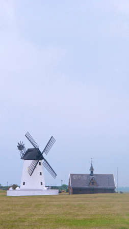 white windmill next to the church with green grass and blue skies in an urban settingの写真素材