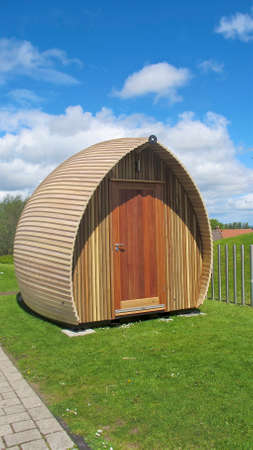 modern wooden glamping style wigwam with grass and cloudy blue skies in backgroundの写真素材