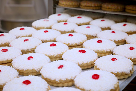 tray full of cakes with coconut topping and cherry on top sat on a baking tray.