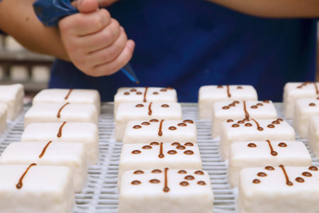 hand prepared iced cakes with dominoes themed chocolate spots being applied.の写真素材
