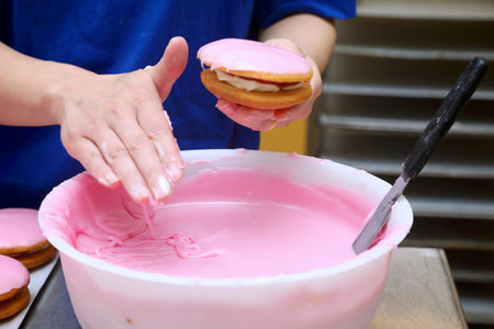 pink icing from a bowl being applied by hand to a jam and cream cake.の写真素材