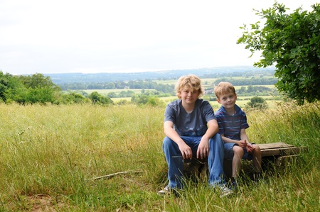 two young brothers resting on a bench in a wild meadowの写真素材