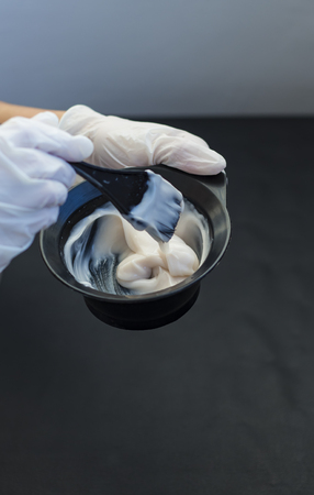 Barber holds a bowl of hair dye on black background with copy spaceの写真素材