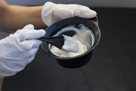 the hairdresser holds the bowl and mixes the hair dye on a black backgroundの写真素材