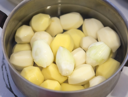 peeled raw potatoes and onions in a pot on the table.の写真素材