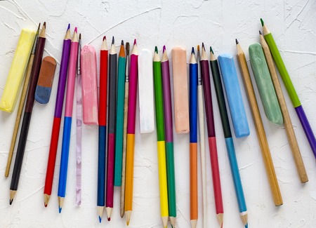 Colored pencils and chalk on white background top view.