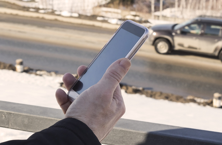 male hand with a smartphone on the background of the road.the concept of this video conversation or photograph.の写真素材