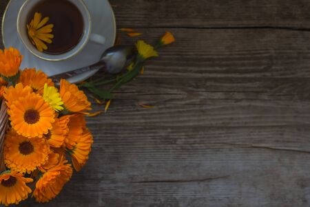 bouquet of calendula with a Cup of tea on a wooden background top view with a copy of space.の写真素材