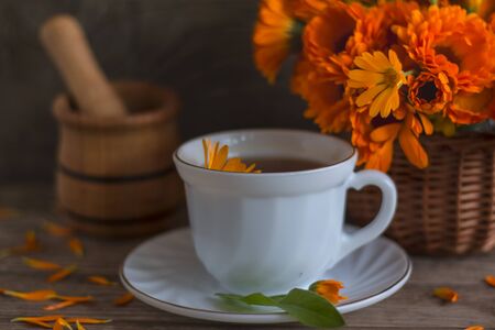 Tea with calendula in a basket on a wooden background and mortar with pestle for grinding herbs.の写真素材