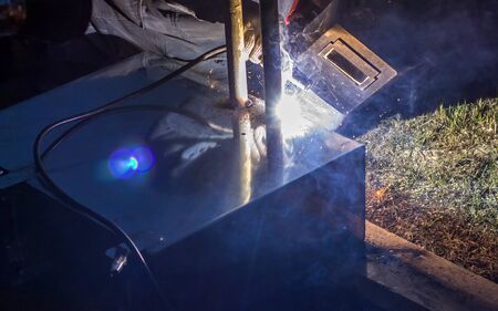 professional welder welds metal parts by electric welding, forming a bright light.