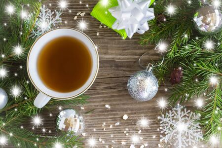 Snowflakes with fir branches and decorations Cup of hot tea and gift on old wooden backgroundの写真素材