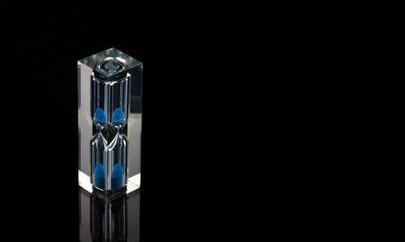 small hourglass with blue sand on dark background with copy space.