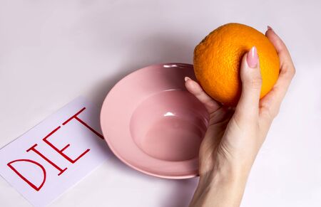 the girl reluctantly goes on a fruit diet, holding an orange over her pink plateの写真素材