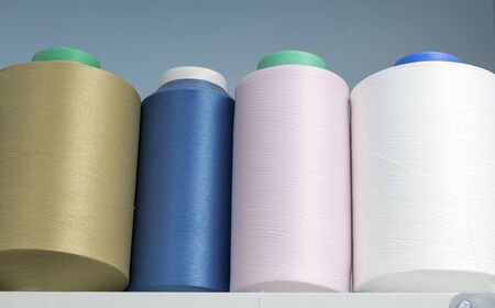 colored elastic threads wound on bobbins are on the shelf in the production.