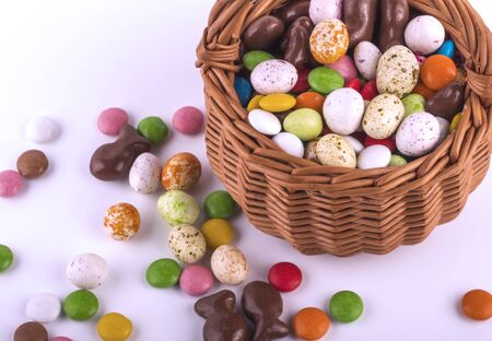 multicolored candy similar to eggs in an Easter basket on a pink background.