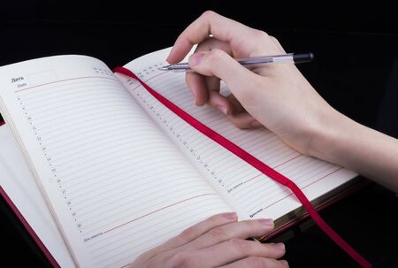 a woman's hand writes with a pen in a notebook on a black background.