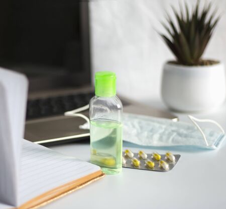 Remote work on the computer during quarantine, on the table a medical mask with antiseptic gel and...