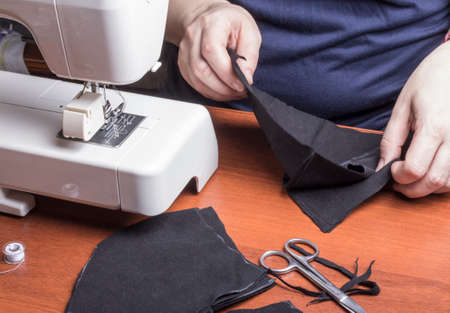 a woman sews a black protective mask to wear outside during quarantine.