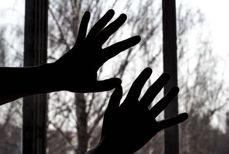 The silhouette of a hand against the background of a day window, a person in quarantine wants to go outsideの写真素材