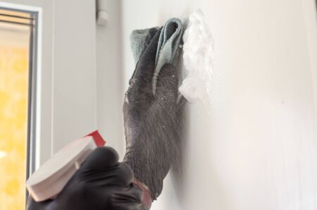 A hand in a black protective glove cleans the wall with a cloth and a special tool. disinfection in...