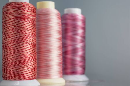 Colored melange threads of red hue on bobbins with a copy of space.