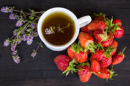green tea with thyme and lots of red strawberries on a wooden background.の写真素材