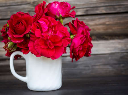 a bouquet of red roses in a White glass on a wooden surface with a copy of the spaceの写真素材