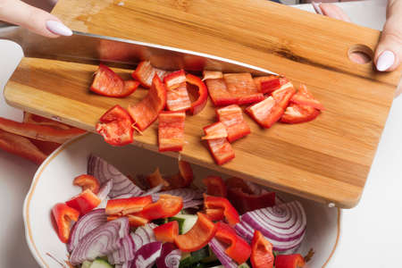 Sliced red sweet pepper on a cutting Board is transferred to a salad bowl.の写真素材