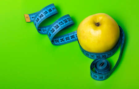 yellow Apple with blue measuring tape on green background diet and sports concept with a copy of the...