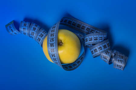 yellow Apple with blue measuring tape on a blue background diet and sports concept.