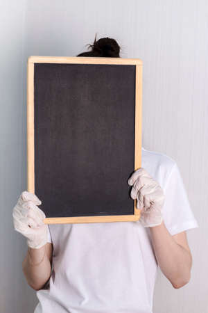 a girl in latex gloves holds an empty black A4 poster on a light background.の写真素材