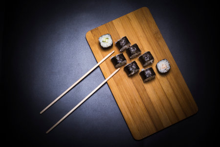 wooden board with rolls and chopsticks on black backgroundの写真素材