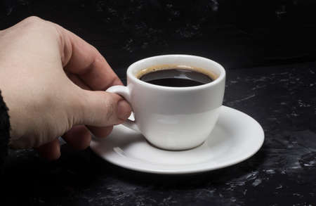 a woman takes a white cup with black aromatic coffee in her hands to enjoy its taste.