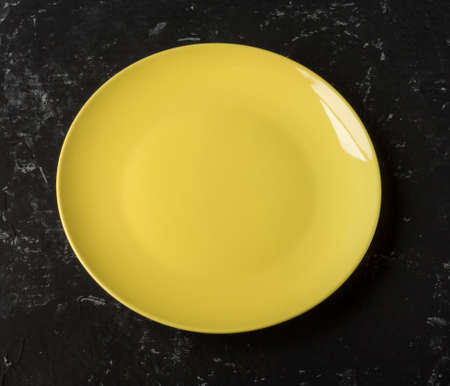 an empty yellow plate on a black textured background.