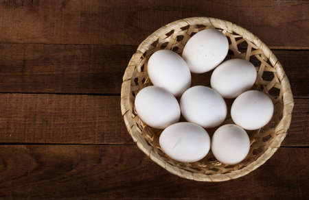 wicker plate with white eggs on a wooden brown background, top view with a copy of the space