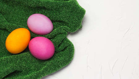 three Easter eggs lay flat on a grass-green tablecloth on a white textured background with a copy of the spaceの写真素材