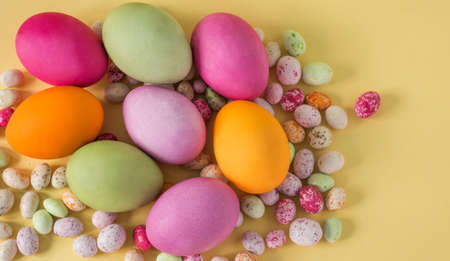 Colorful Easter eggs with colored candies on a yellow background top view flat lay.