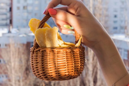 dried mango in a wicker basket in the hands of a girl against the background of a winter city, the concept of vitamins in winter.の写真素材