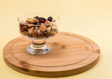 nuts and dried fruits in a glass vase on a yellow background with a copy of the space.の写真素材