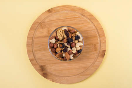 nuts and dried fruits in a glass vase on a yellow background flat lay.
