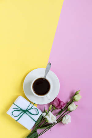 white cup with coffee and flowers and a gift on a yellow-pink background with a copy of the space,...