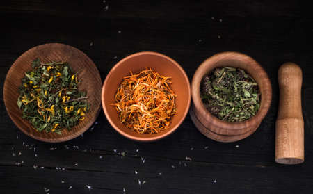 dry medicinal herbs in different containers on a black wooden background.の写真素材